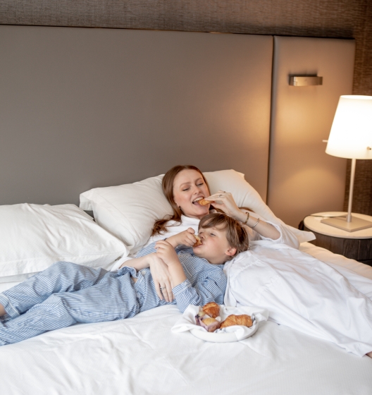 Mother and son enjoy snacks in hotel room bed