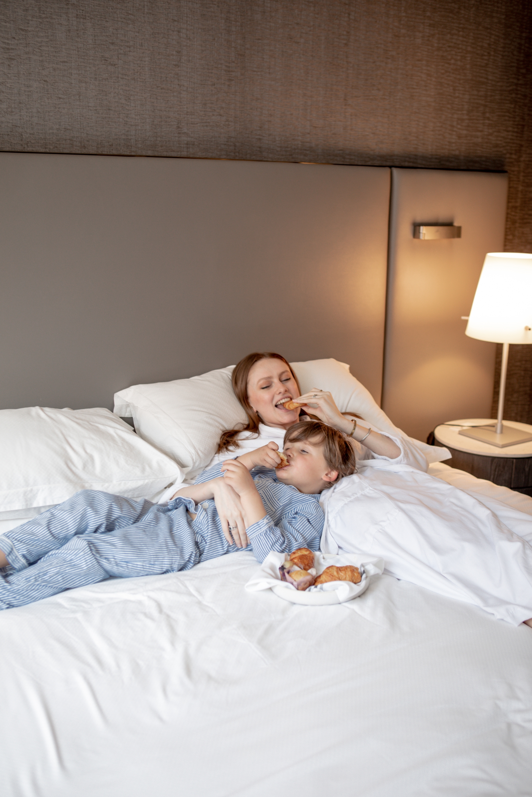 Mother and son enjoy snacks in hotel room bed