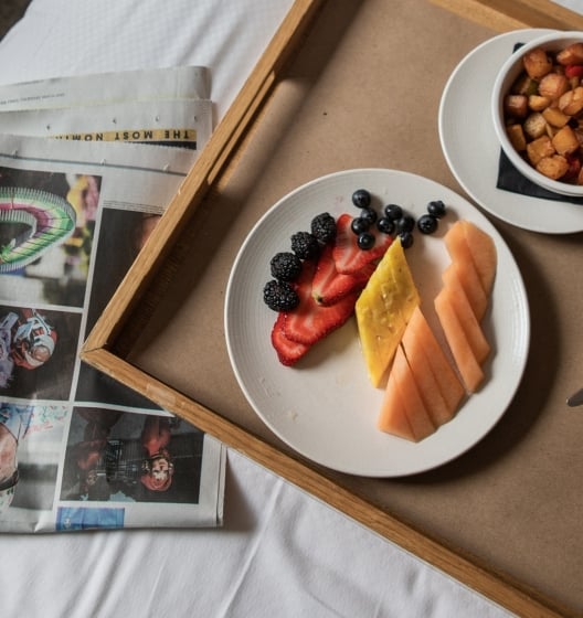 A woman in a robe sitting on a bed with a tray of food, enjoying room service in a Tribeca Hotel