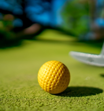 Mini Golf yellow ball with a bat near the hole at sunset