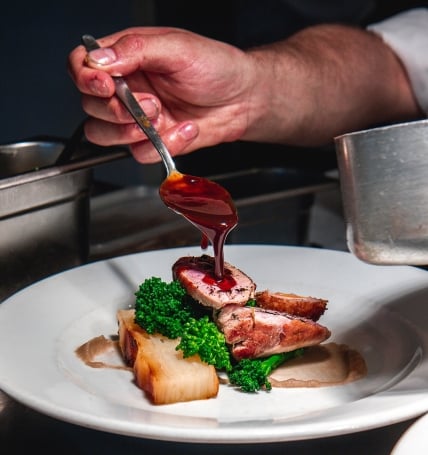 chef hand pouring gravy onto roast beef plated food dinner