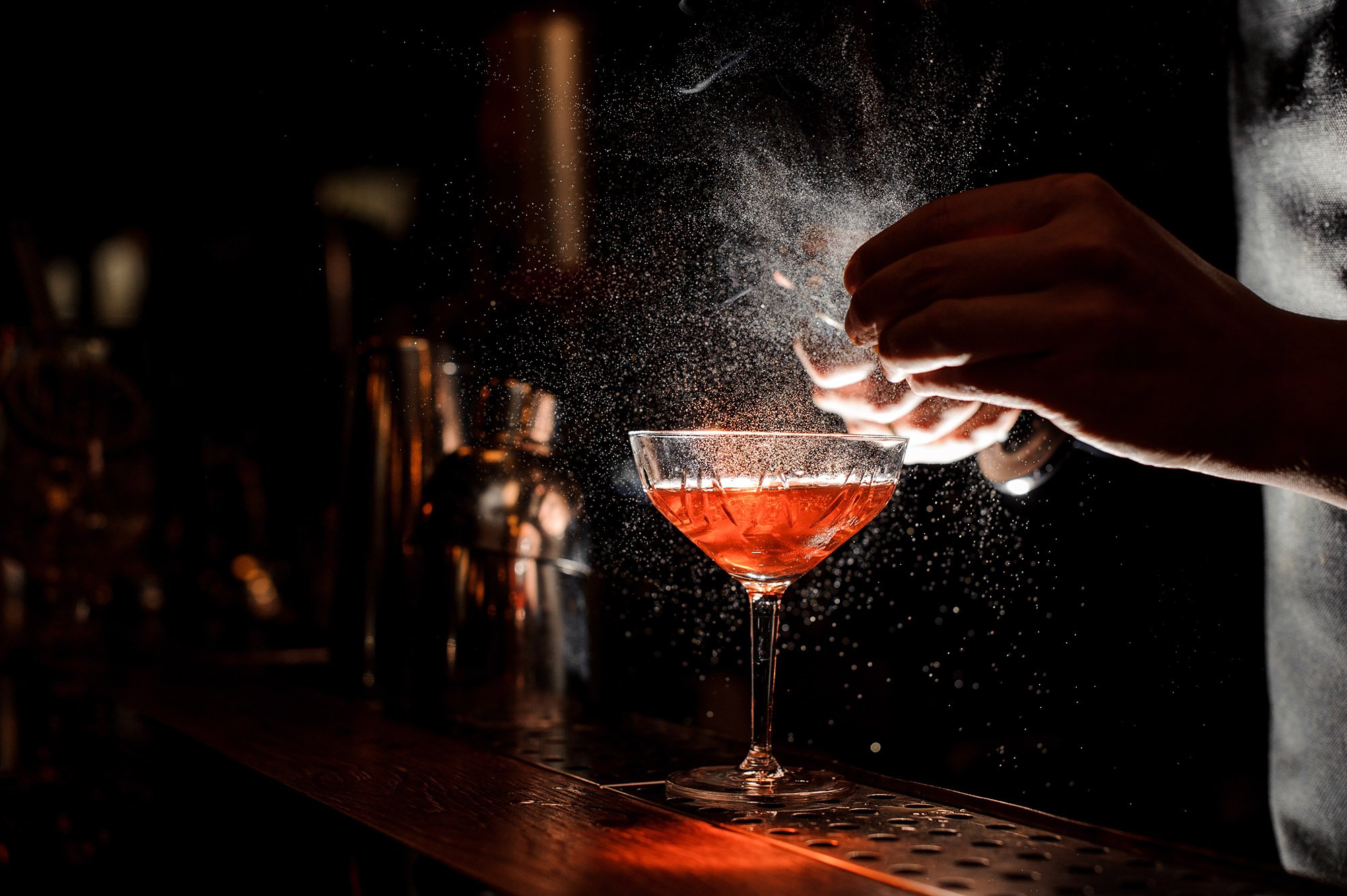 Bartender's hands sprinkling the juice into the cocktail glass