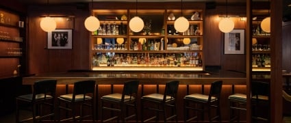 Galerie Bar in the Smyth Hotel in NY; A spacious bar with a lengthy counter and a handful of chairs, inviting patrons to relax and enjoy their drinks.