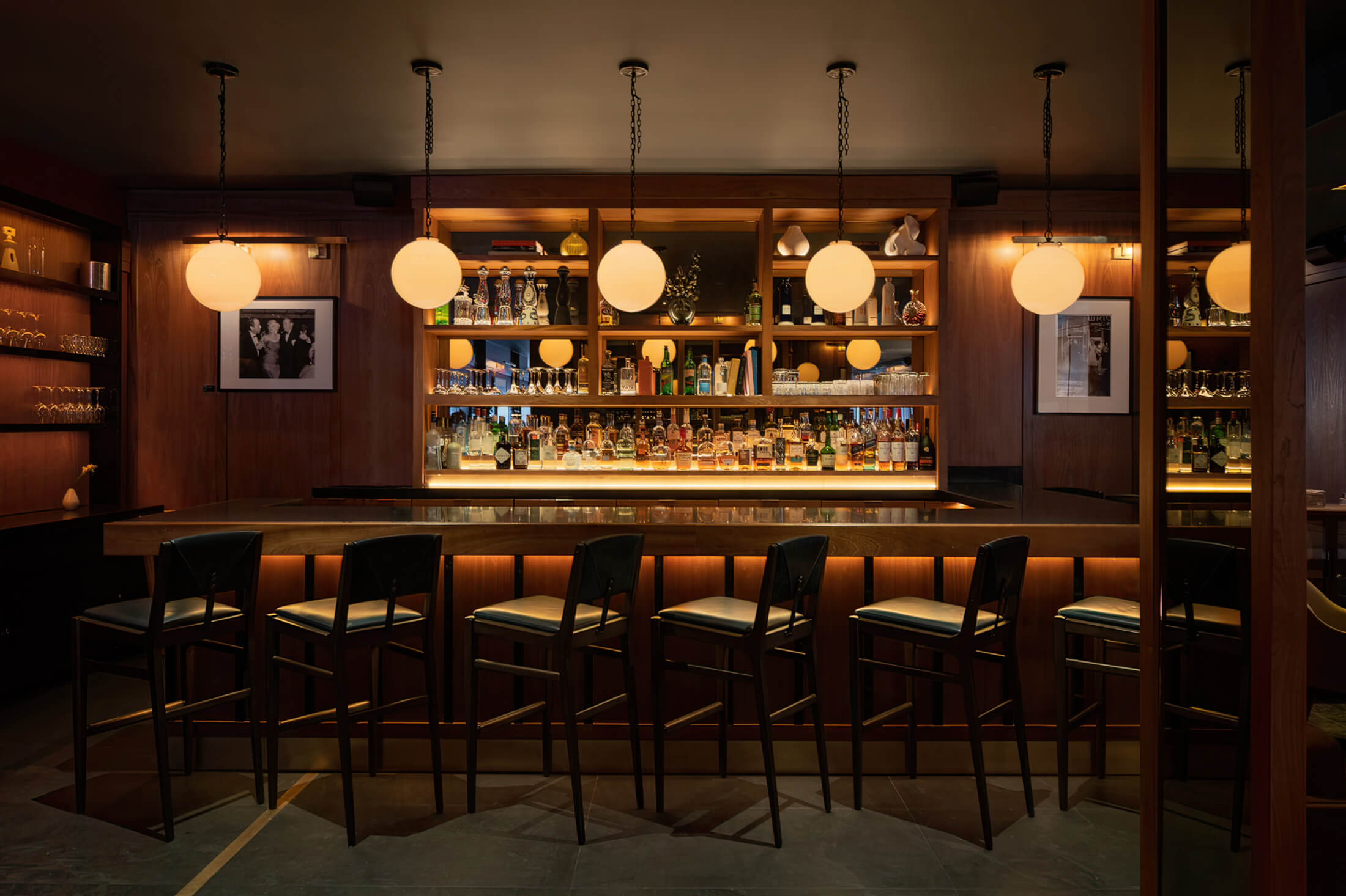 Galerie Bar in the Smyth Hotel in NY; A spacious bar with a lengthy counter and a handful of chairs, inviting patrons to relax and enjoy their drinks.