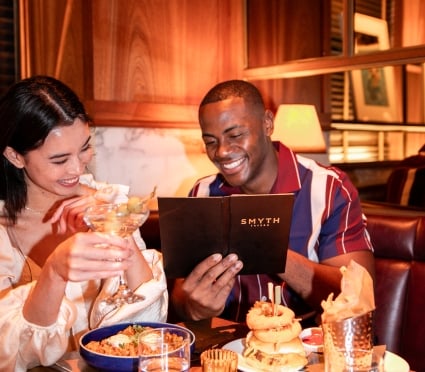 couple reading Smyth Taverna restaurant menu; Woman and man sitting ad laughing at Taverna Restaurant in Tribeca New York