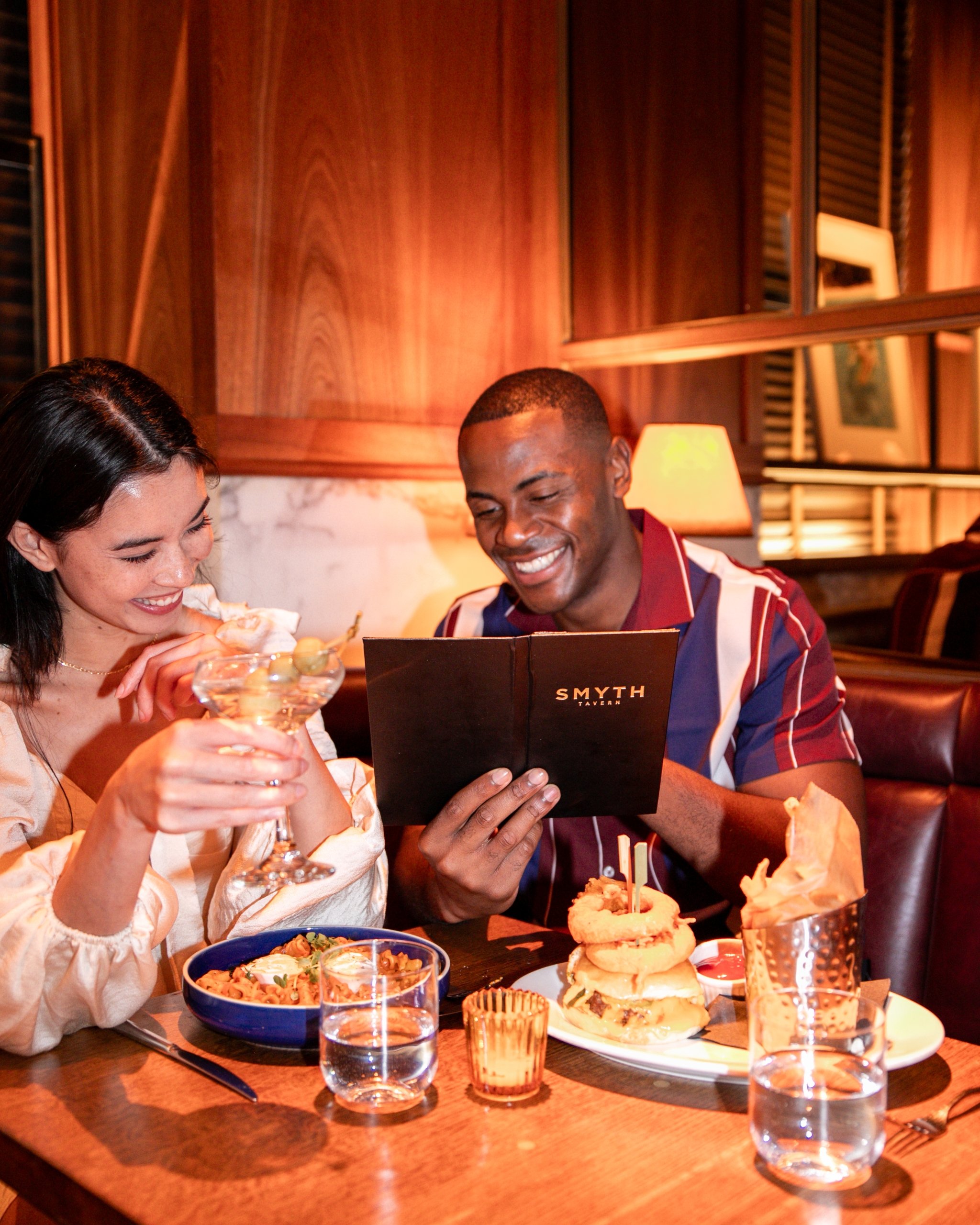 couple reading Smyth Taverna restaurant menu; Woman and man sitting ad laughing at Taverna Restaurant in Tribeca New York