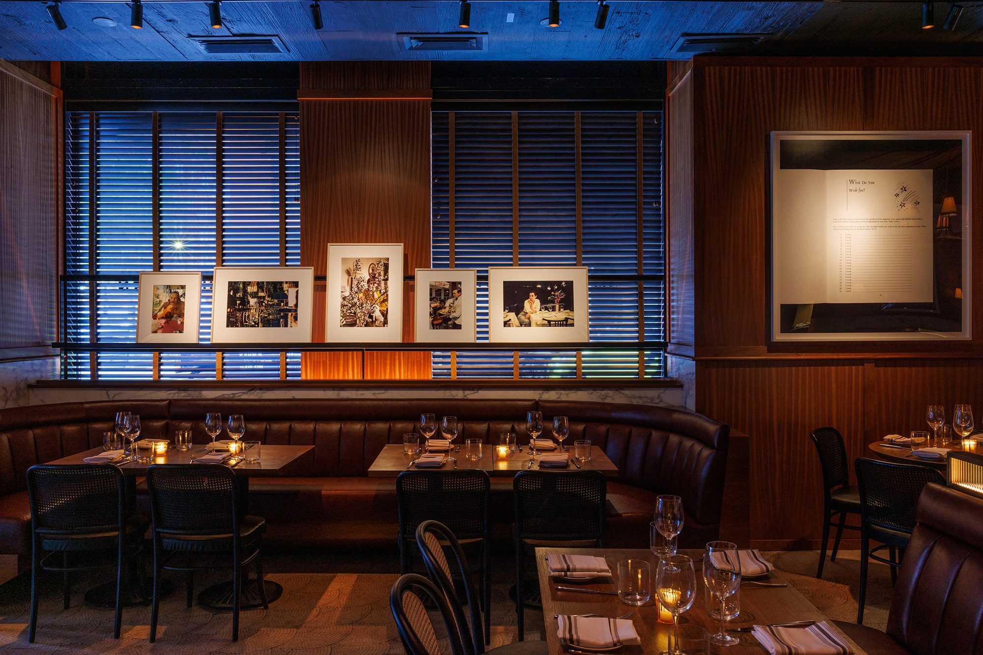 A dimly lit dining area with a booth and tables set for dinner, adorned with artwork and candlelight.