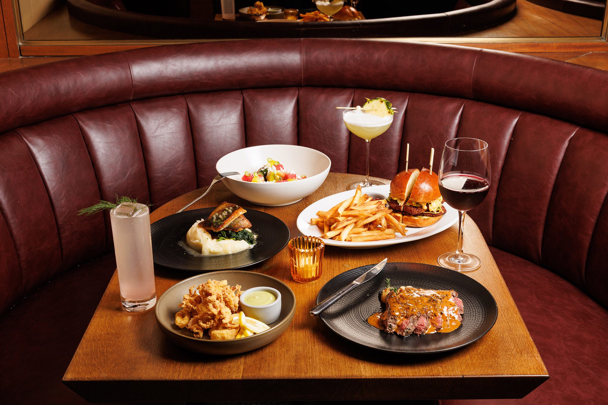 A table set with various dishes and drinks in a booth.