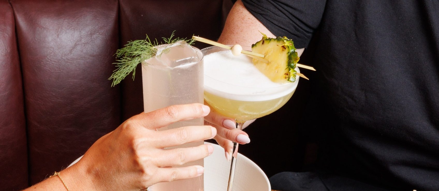Two hands holding up cocktails with garnishes