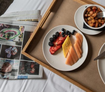 A woman in a robe sitting on a bed with a tray of food, enjoying room service in a Tribeca Hotel