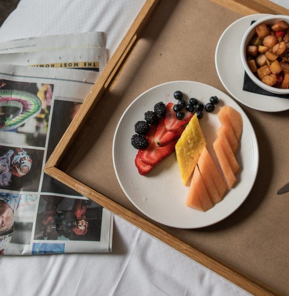 A woman in a robe sitting on a bed with a tray of food, enjoying room service in a Tribeca Hotel