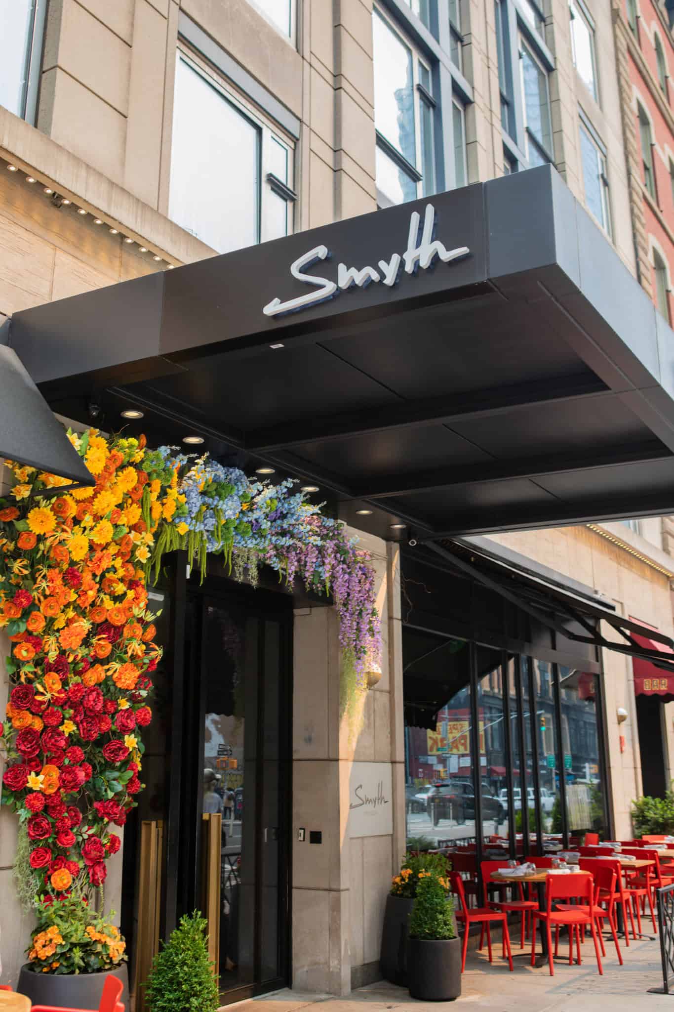 A hotel entrance with a black awning and colorful flowers